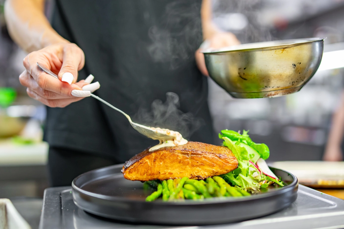 Chef preparing salmon dish with sauce