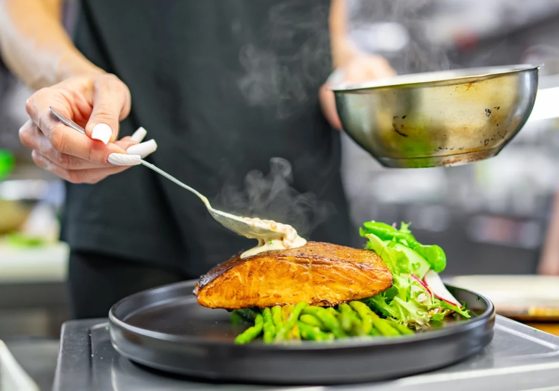 Chef preparing salmon dish with sauce